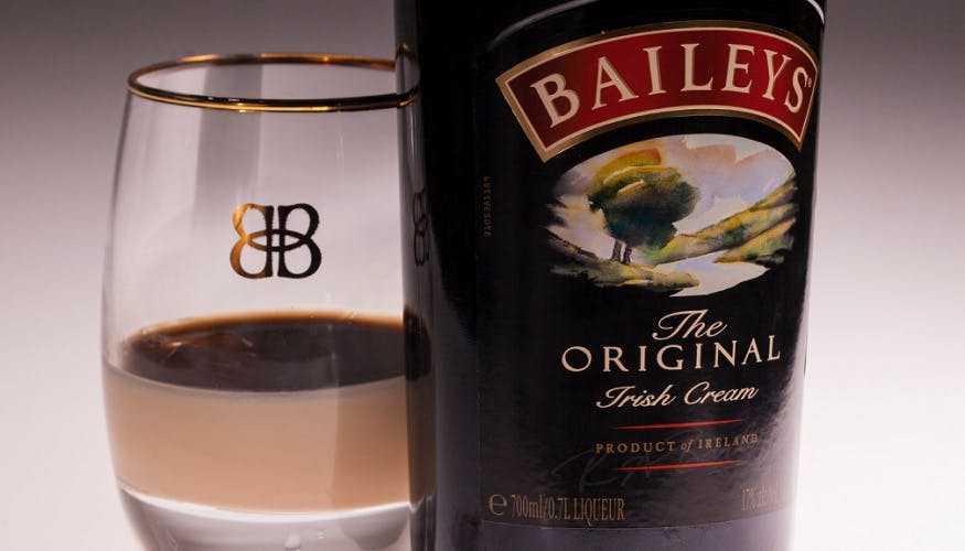 Close-up photograph of a bottle of Baileys alongside a glass that has a small amount poured into it.