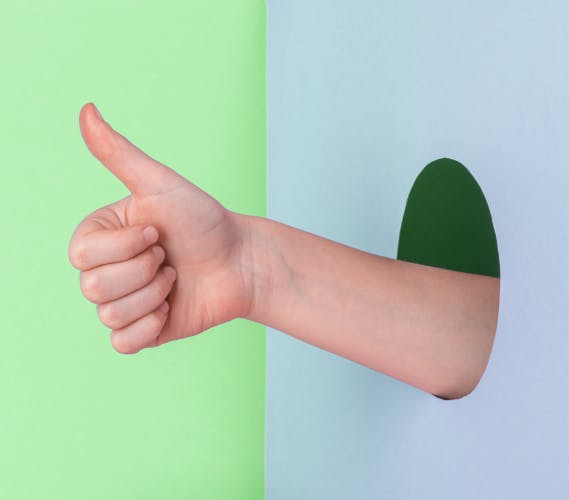 Hand showing a thumb up through a hole in the wall